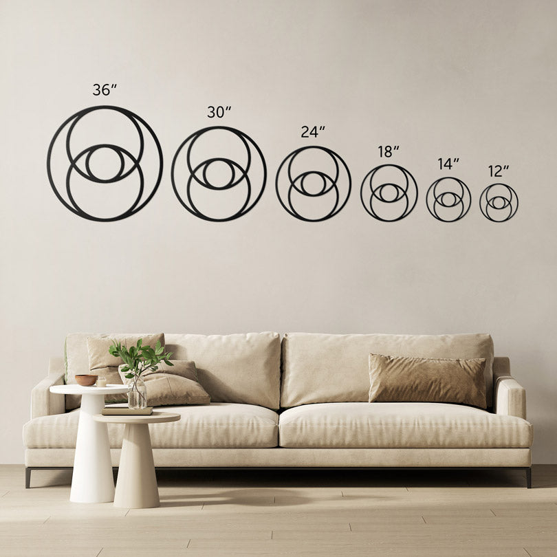 Vesica Pisces metal wall art in 6 sizes showed side by side for comparison. The largest one on the left is 36 inch, then 30 inch, 24 inch, 18 inch, 14 inch and 12 inch. The sizes are shown in a living room above a beige sofa with brown cushions.