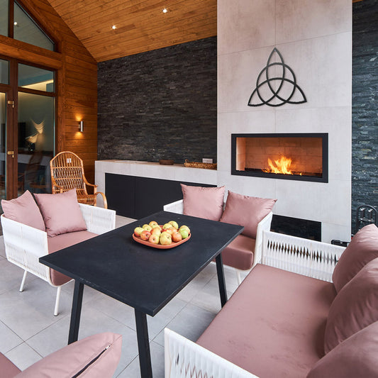 Home Decor Art Wall Sacred Geometry Triquetra Wall Metal Art in black, is displayed In the living room, below is a fireplace, with a burning fire, a sitting area with pink sofas, a black table with a plate of apples.