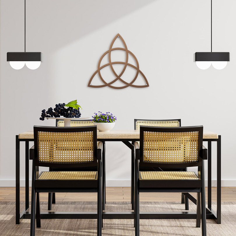 Home Decor Art Wall Sacred Geometry Triquetra Wall Metal Art in copper, is hanging In on the wall in a  warm and modern dining room, with a black wooden table, flower decorations on the table and two lamps hanging from the ceiling.