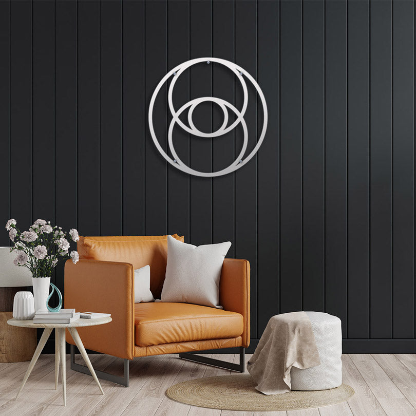 Sacred Geometry Home Decor The Vesica Pisces Metal Wall Art in white is displayed in a black wall with stripes, an orange single sofa, white decorative pillows, a parquet floor, a round straw rug, a small white table with a vase with flowers on it.