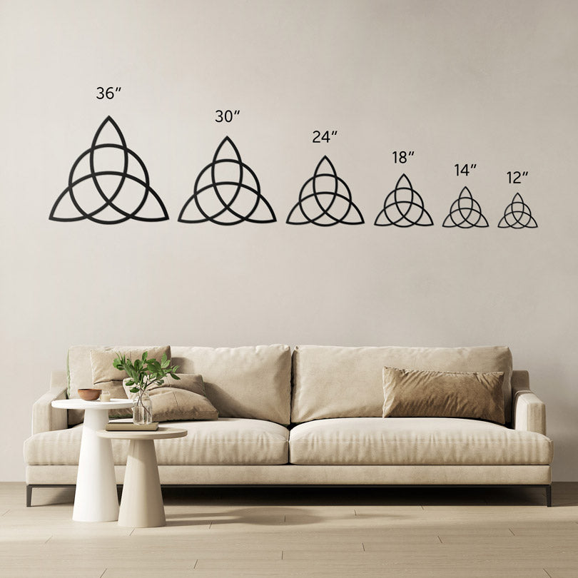 Triquetra metal wall art in 6 sizes showed side by side for comparison. The largest one on the left is 36 inch, then 30 inch, 24 inch, 18 inch, 14 inch and 12 inch. The sizes are shown in a living room above a beige sofa with brown cushions.